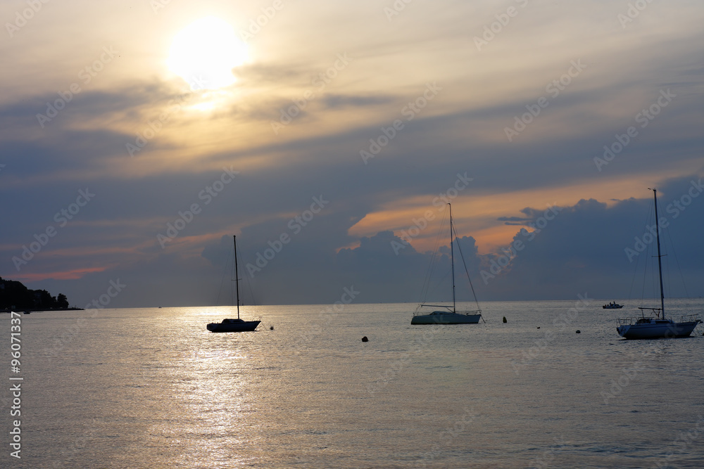 Three sailboats on open sea in a summer at sunset time