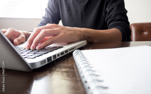 Close up of business man's hands working on laptop computer with notebook on wooden desk