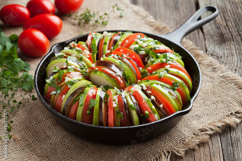 Raw vegetable ratatouille in cast iron frying pan preparation recipe on vintage wooden table background. Healthy organic vegan oven baked food photo