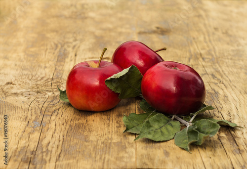 Three red apples with leaves on a light wooden background