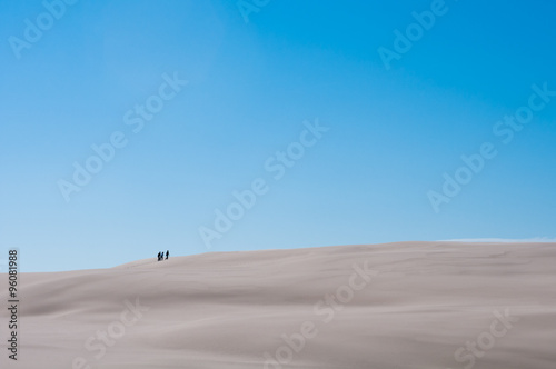 Three People On Sandy Dune With Blue Sky Background