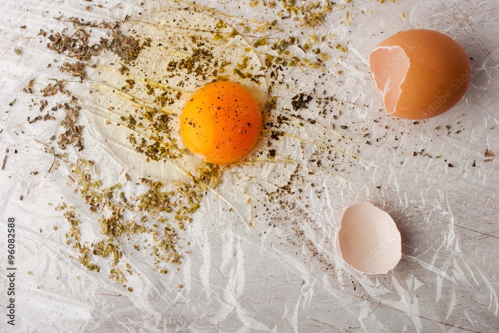 Broken egg with herbs mix on the white table Broken egg with herbs mix on the white table