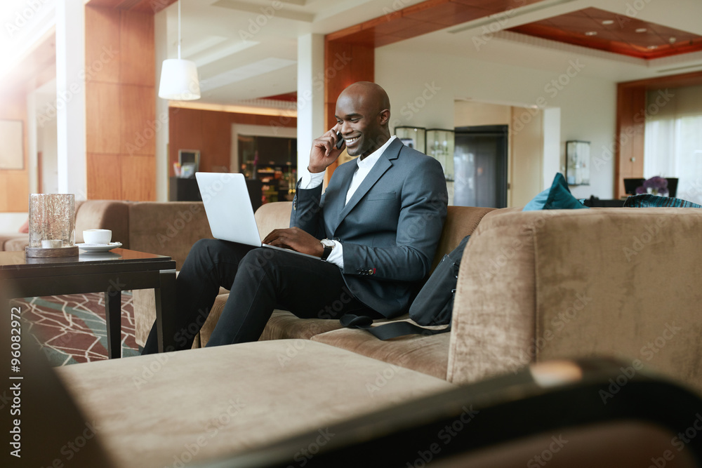 Happy businessman in hotel lobby using cell phone and laptop Happy businessman in hotel lobby using cell phone and laptop