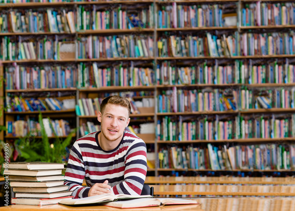 Smiling male student with open book working in a library Smiling male student with open book working in a library