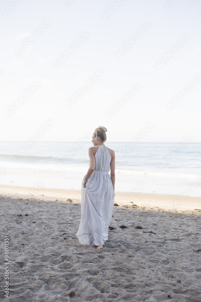 Blond woman wearing a long dress standing on a sandy beach. Blond woman wearing a long dress standing on a sandy beach.