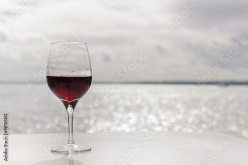 One glass of red wine with tears against tranquil sparkling sea water