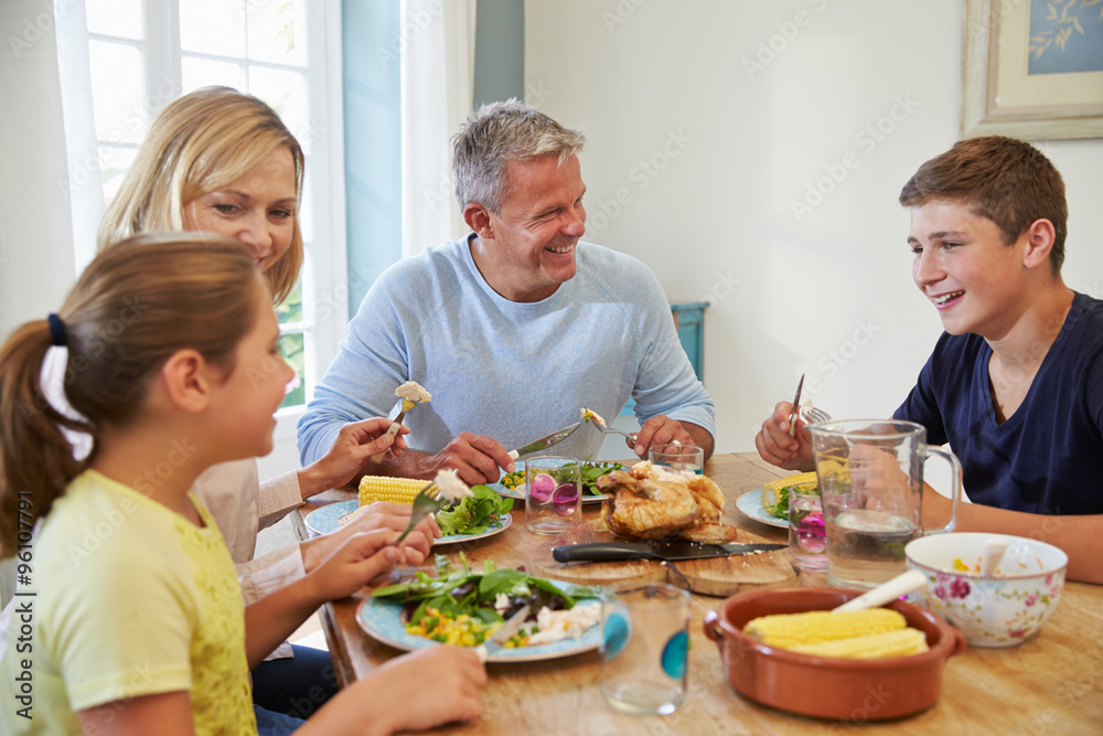 Family Sitting At Table Enjoying Meal At Home Together