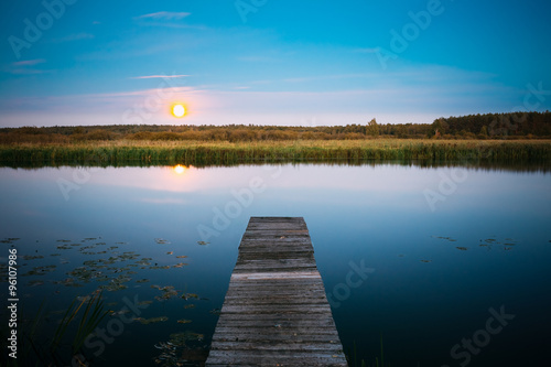Moonrise over river lake pond in summer evening. Wooden boards p