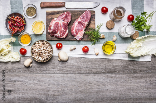 Ingredients for cooking pork steaks on the cutting board, on a napkin, vegetables, mushrooms, lettuce, spices and herbs on wooden rustic background top view border, place for text