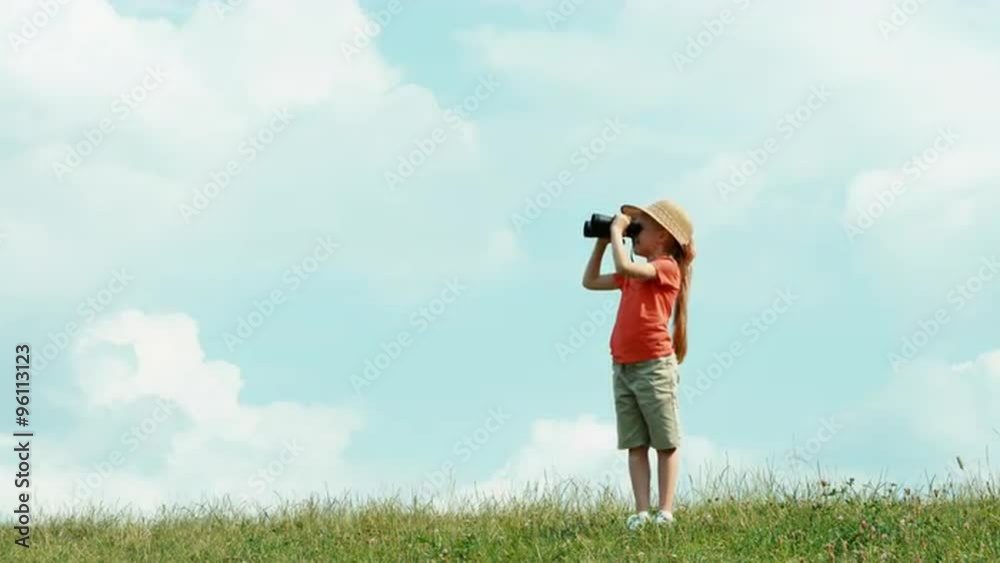 Girl through binoculars watching wildlife and looking at camera. Girl standing on the hill against the sky Girl through binoculars watching wildlife and looking at camera. Girl standing on the hill against the sky