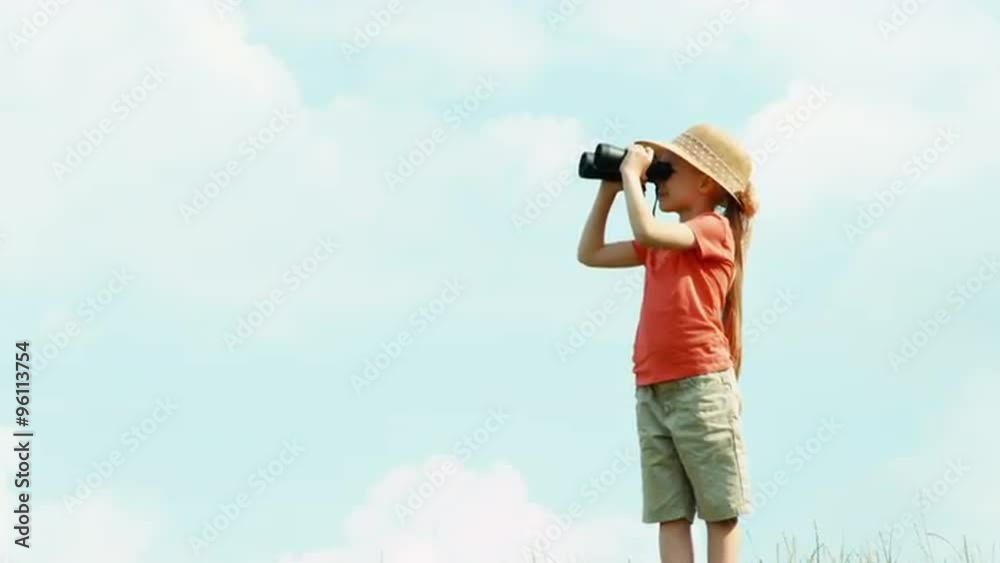 Girl through binoculars watching wildlife. Girl standing against the sky and waving hand Girl through binoculars watching wildlife. Girl standing against the sky and waving hand