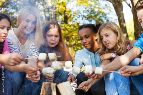 Happy friends hold marshmallow sticks near bonfire