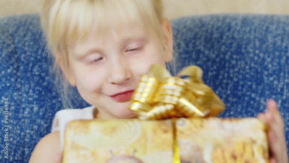 Blonde girl looking at a box with a Christmas present, laughs Blonde girl looking at a box with a Christmas present, laughs