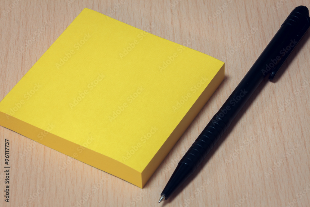 black pen,yellow paper on wood table background. black pen,yellow paper on wood table background.