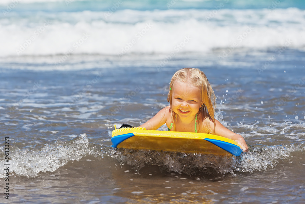 Little baby girl - young surfer with bodyboard has a fun on small sea  waves. Active family