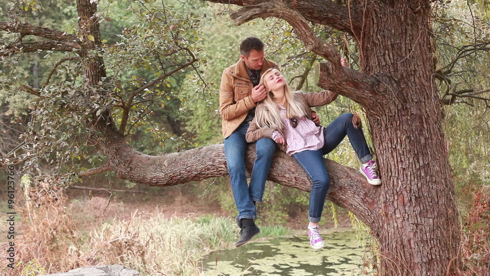 Couple in love sitting on big old tree in forest and hugging Couple in love sitting on big old tree in forest and hugging
