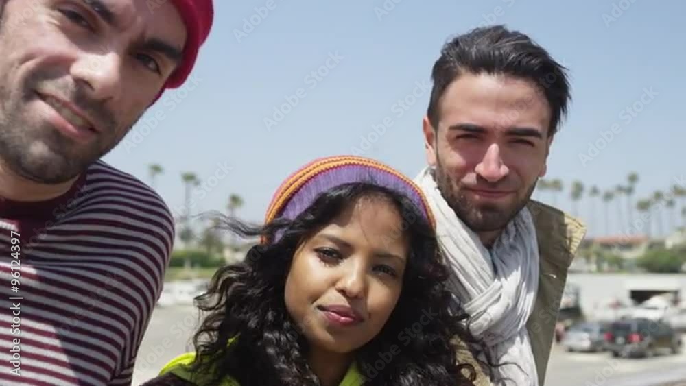 Three hip ethnic diverse friends staring at camera panning at the beach Three hip ethnic diverse friends staring at camera panning at the beach