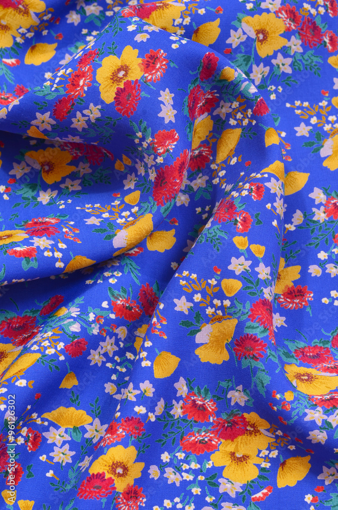 Floral pattern crumpled on fabric. Red and yellow flowers print on blue as background.