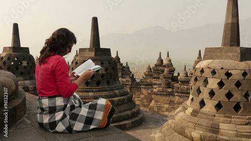 woman tourist reading a guidebook in an Indonesian Borobudur Buddhist temple wide shot	 photo