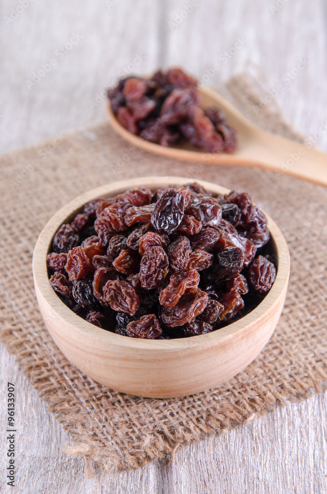 dry raisins in wooden bowl and spoon on white wooden table dry raisins in wooden bowl and spoon on white wooden table
