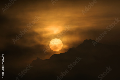 Rising sun behind fog and mountain range