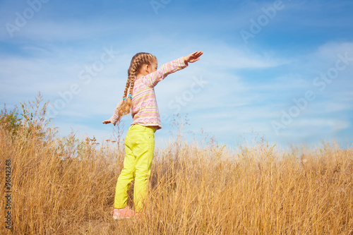 Little girl in bright clothes standing against the sky