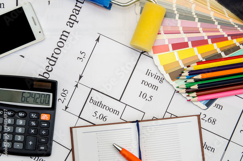 Paintbrushes and colorful paint samples on house plan with pencil, notebook, tea as background