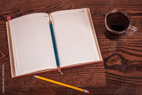 cup of tea, pen, opened organizer on the wooden table.  Blue toned
