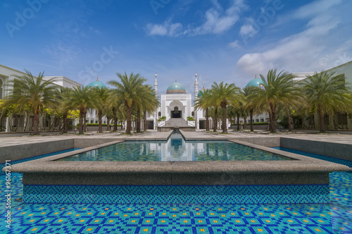 The white of Mosque Albukhary located in Alor Star, state of Kedah, Malaysia with its fountain and squares in the foreground and blue sky with clouds in the background.