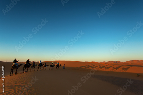 Sillhouette of camel caravan going through the desert at sunset