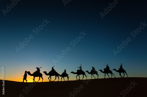 Sillhouette of camel caravan with happy peopple going through th