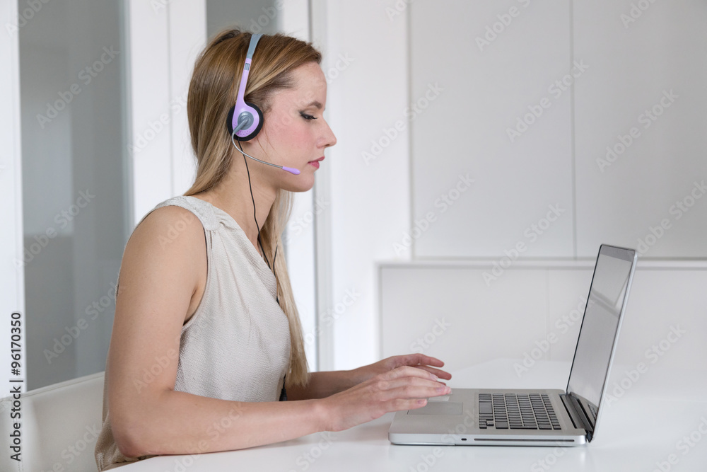 Attractive blonde woman with headset working on a laptop.