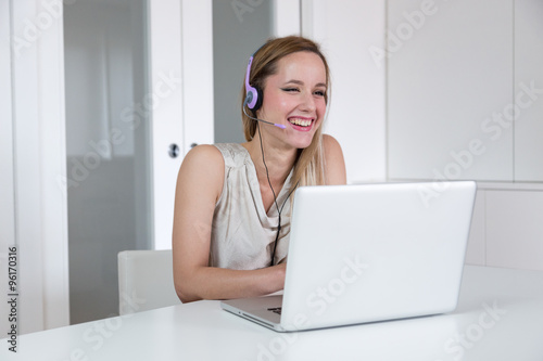 Attractive smiling blonde woman with headset working on a laptop.