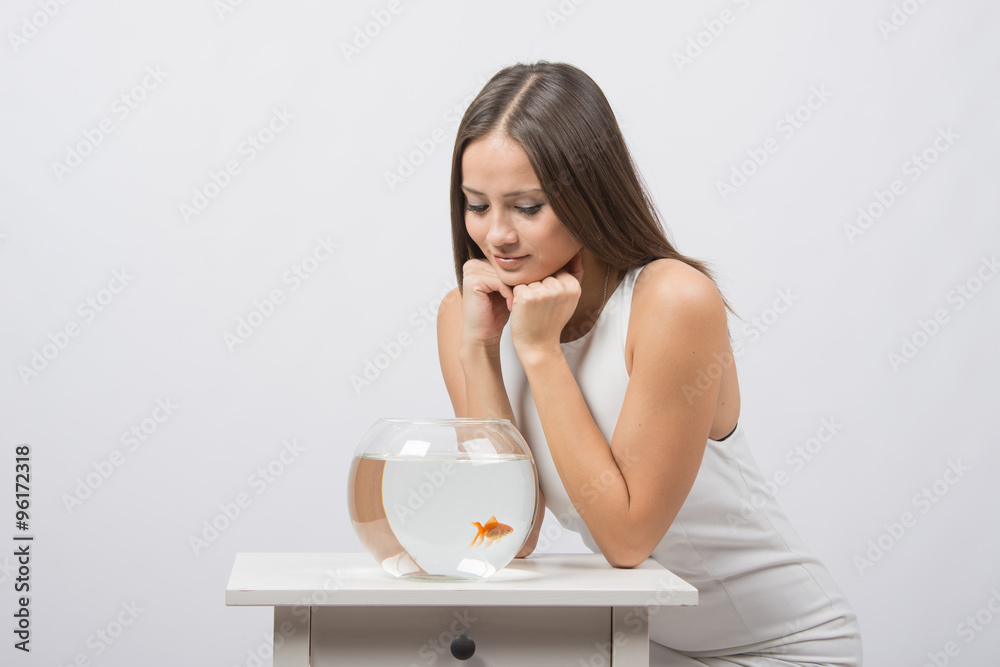 The girl sits near the aquarium with goldfish and looks at it The girl sits near the aquarium with goldfish and looks at it