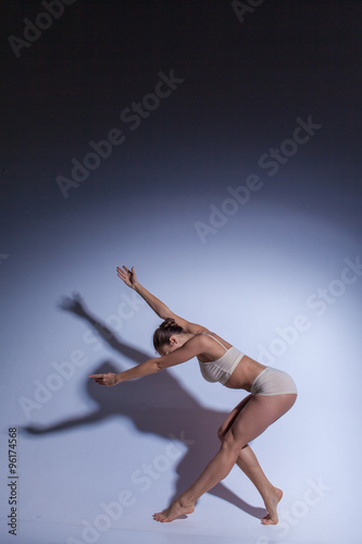 Young beautiful dancer in beige swimwear dancing on lilac background