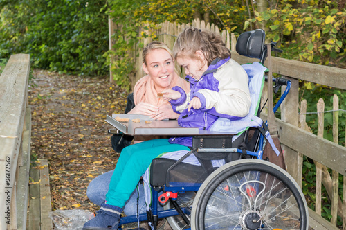 Disabled girl in a wheelchair relaxing outside / Disabled child relaxing outside with help from a care assistant
