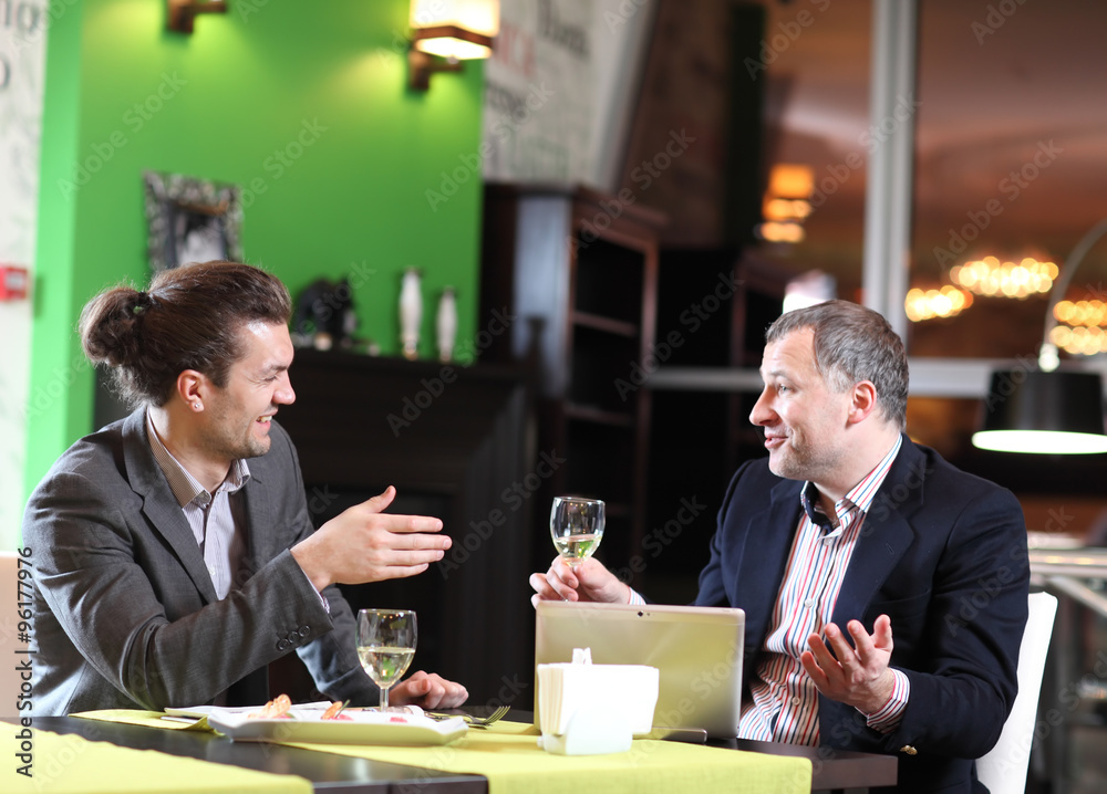 Two smiling business men eat at restaurant