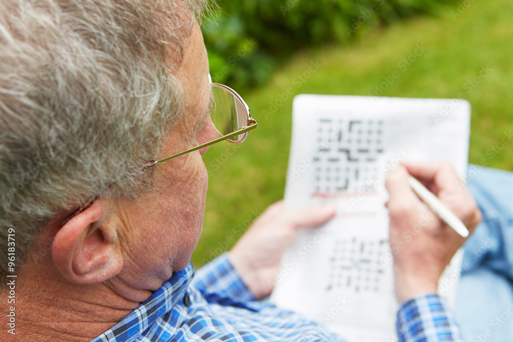 Naklejka premium Senior Man Doing Crossword Puzzle In Garden