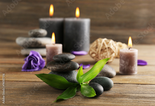Relax set contains alight wax candles with flowers and pebbles on wooden background  focus on green leaf