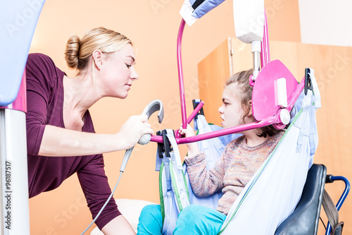 Disabled girl being lifted into wheelchair / Disabled girl being lifted into wheelchair using a lift with help from a care assistant
