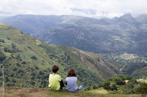 Niños sentados sobre la hierba contemplando las montañas
