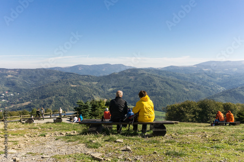 Mature couple resting on a bench in the mountains on a sunny day - rear view - beautiful mountain landscape