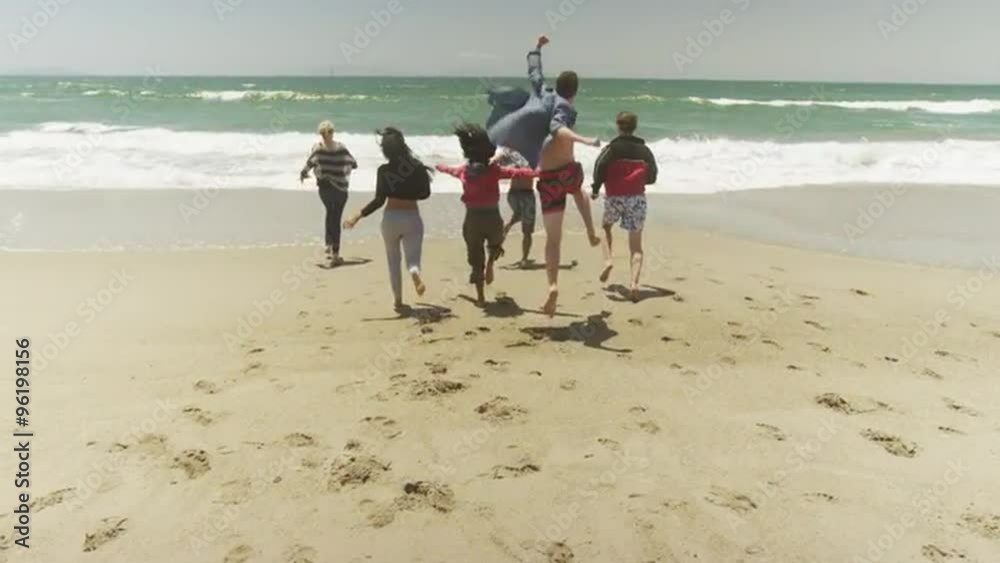 Group of young multi ethnic friends running into water at the beach