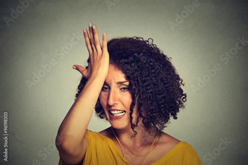 middle age woman slapping hand on head to say duh made mistake photo