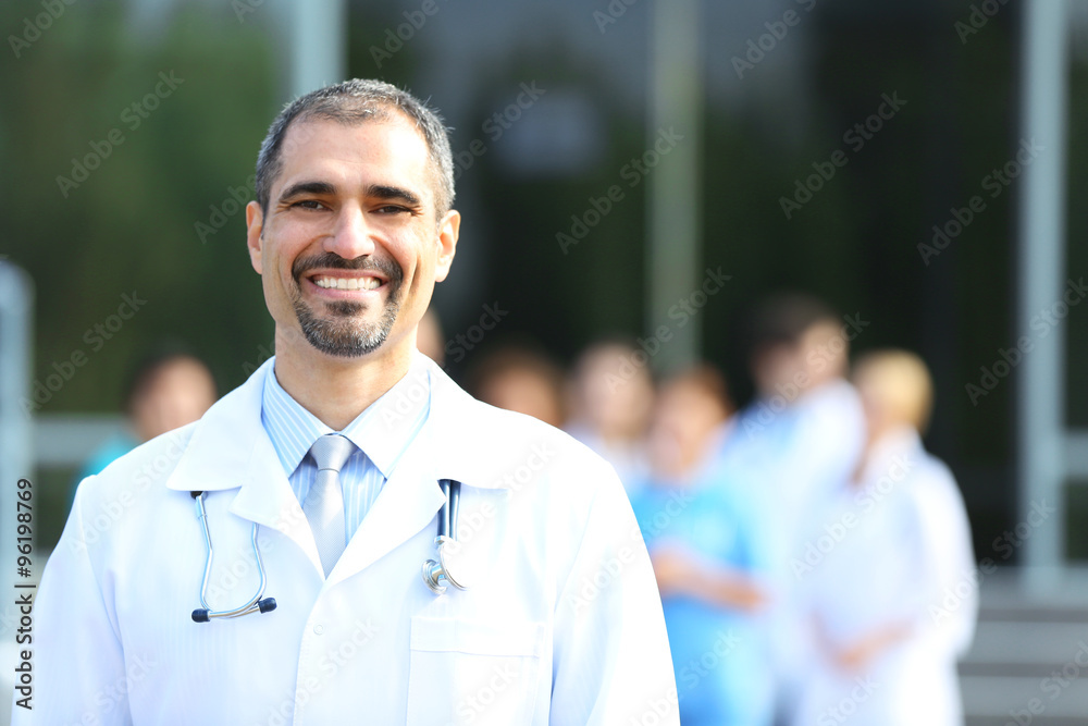 Happy doctor with medical stuff behind standing against clinic entrance Happy doctor with medical stuff behind standing against clinic entrance