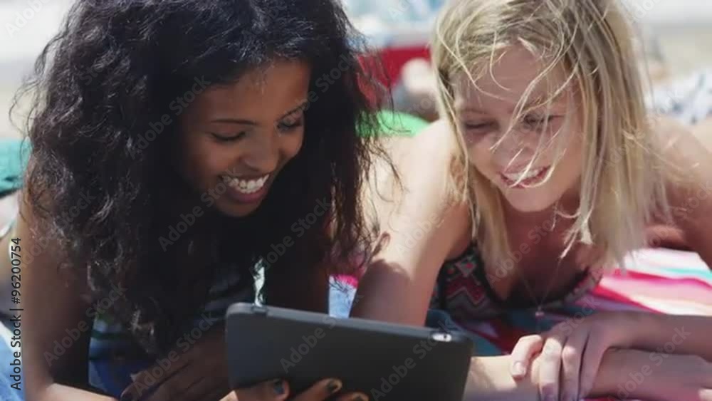 Happy group of young interracial friends looking at tech on the beach