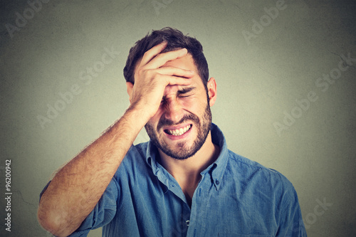 Portrait stressed man suffering from headache isolated on gray wall background