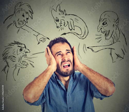 Stressed young man covers his ears with his hands evil guys pointing fingers at him