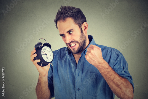 angry young man screaming at alarm clock, running late