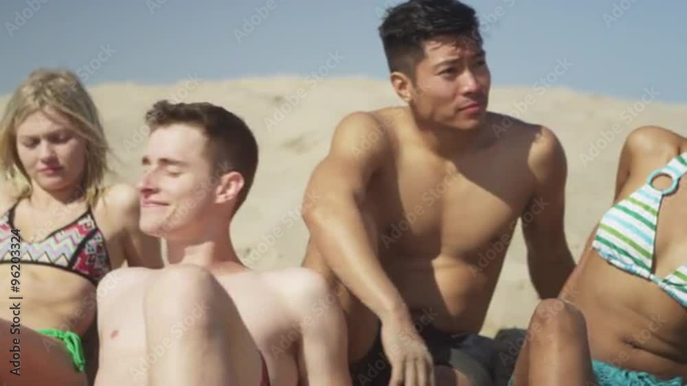Authentic young group of multi ethnic friends sitting in the sand talking Authentic young group of multi ethnic friends sitting in the sand talking